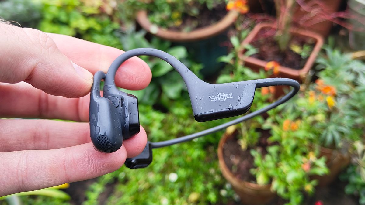 Shokz OpenRun Pro 2 in-ear headphones held in hand above garden plants