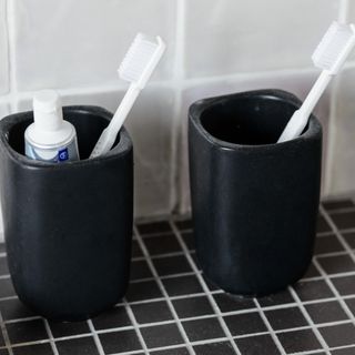 Two cups with toothbrushes and toothpaste on black tiles