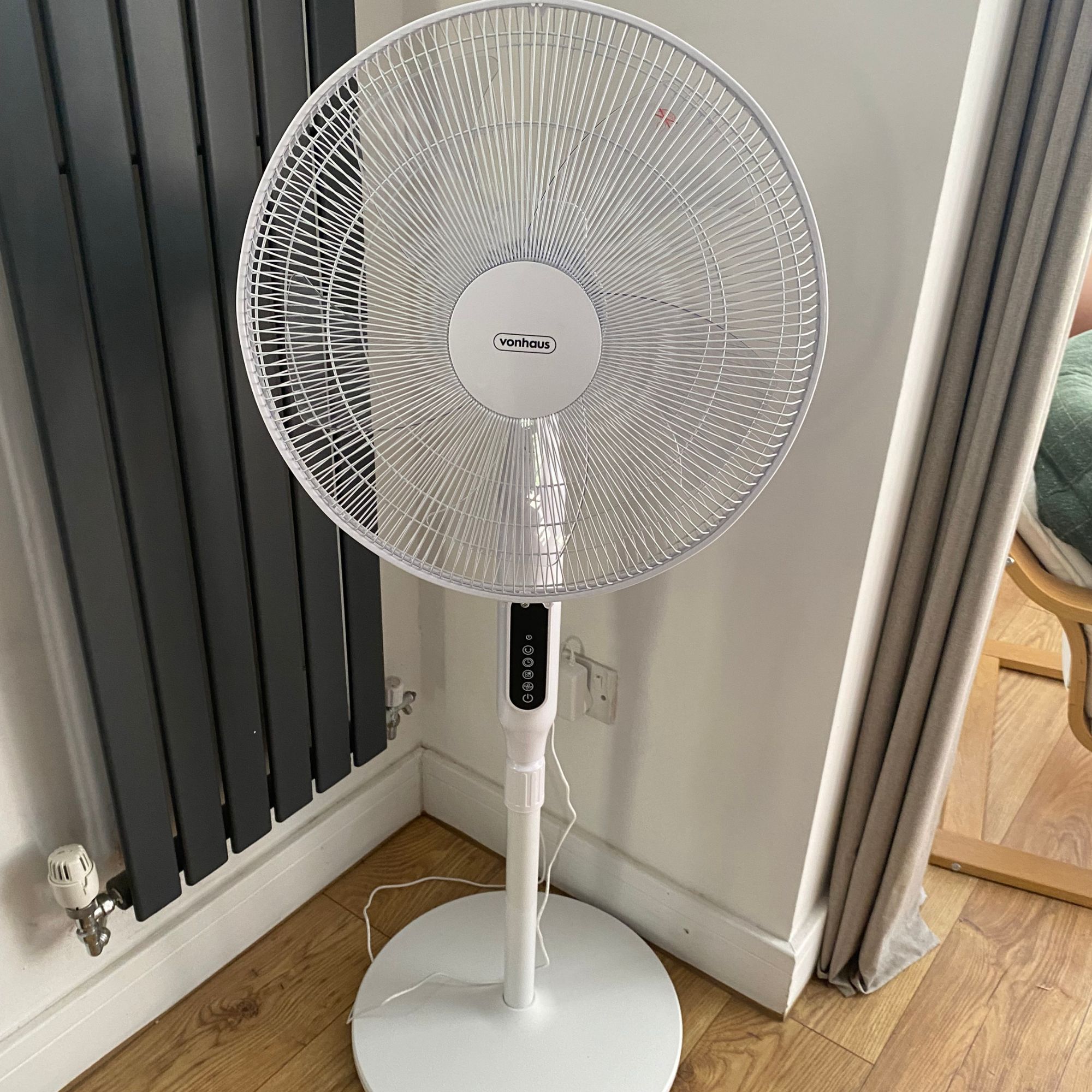The Vonhaus 16'' pedestal fan at it's lowest height in the corner of a room next to a vertical radiator