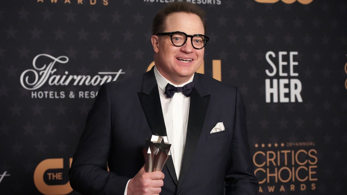 Brendan Fraser stands dressed in a black tuxedo, holding his Critic&#039;s Choice Award. 