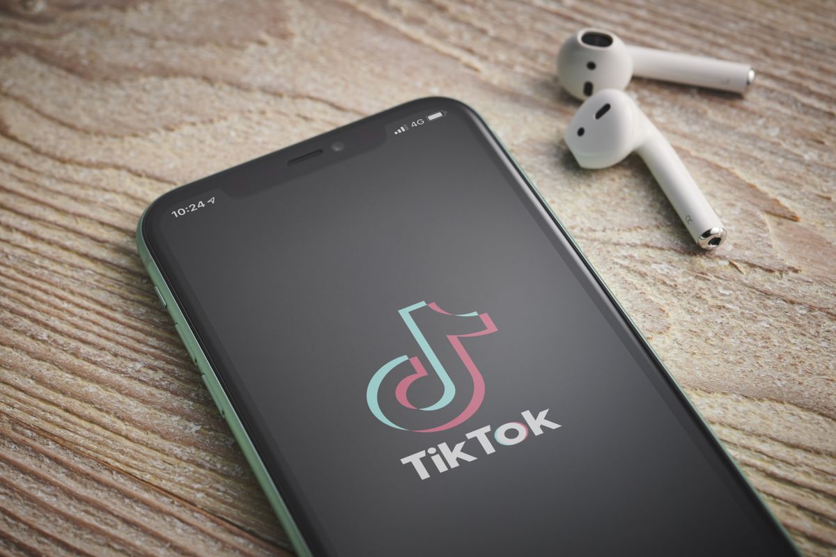 A smartphone displaying the TikTok logo, on a wooden table with a pair of headphones