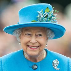 Queen Elizabeth wearing a turquoise hat and coat and smiling