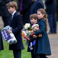 Prince George, Princess Charlotte and Prince Louis wearing blue coats and holding stuffed animals and flowers standing outside church on Christmas Day 2024