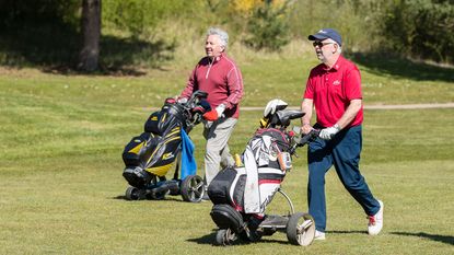 Two golfers using an electric trolley on a golf course