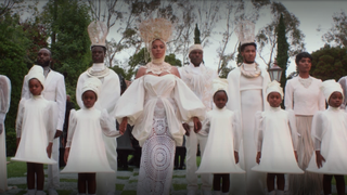 Beyoncé stands alongside a group of men, women and children dressed in all white in a scene from 'Black is King'