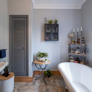 Bathroom with grey cupboard, wooden side table, wooden shelves, bath and basin.
