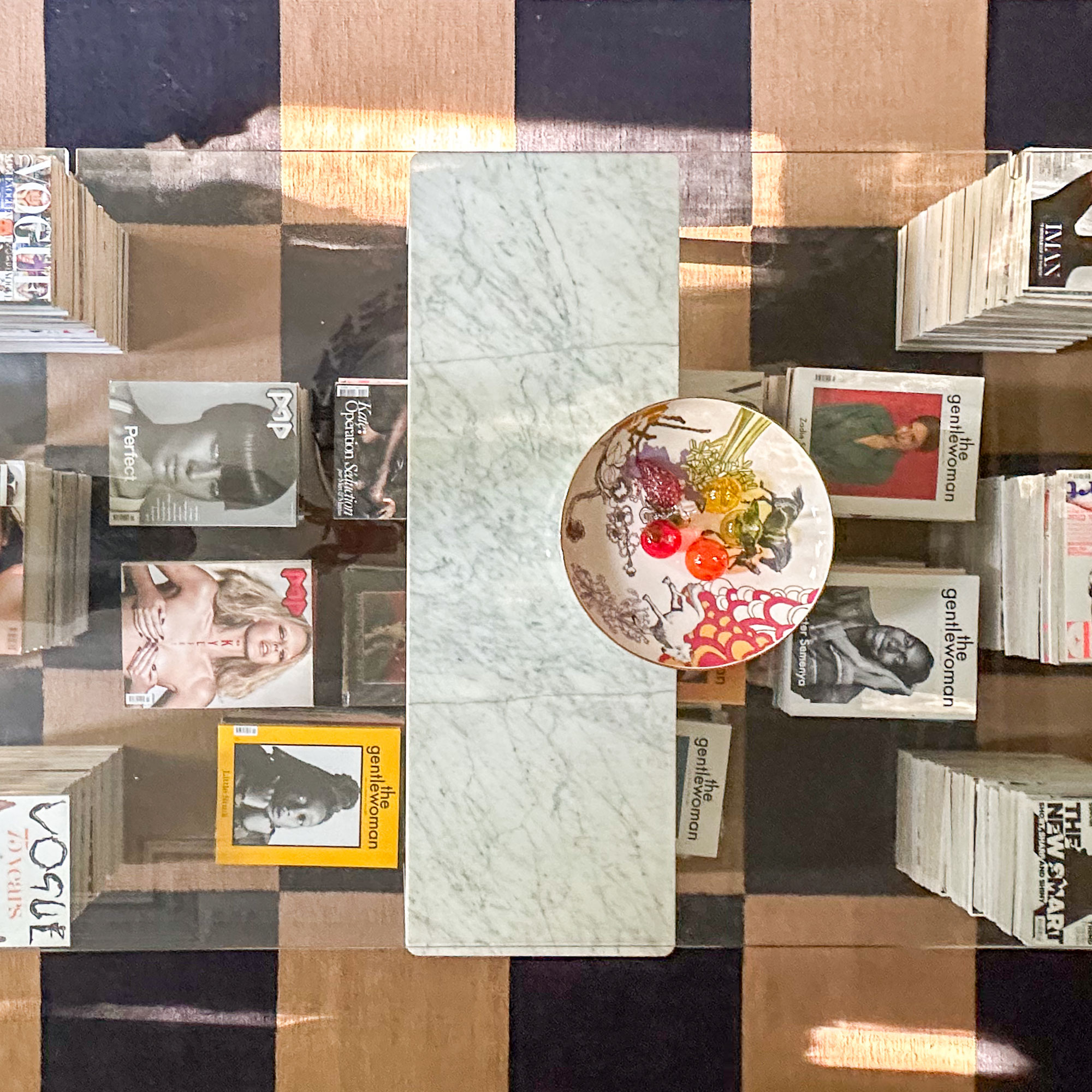 Glass topped coffee table propped up with marble and stacks of magazines