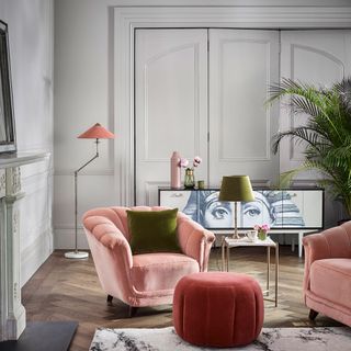 grey walled living room with a wooden floor decorated with pink sofa chairs, a green house plant and a modern chest drawer