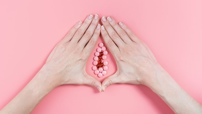 hands and pills in shape of vagina on pink background