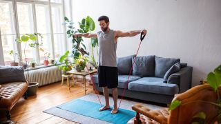 Man performs resistance band lateral raise exercise in his living room 