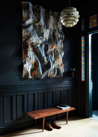 A dark blue entryway with a wooden bench and original glass detailing in the door