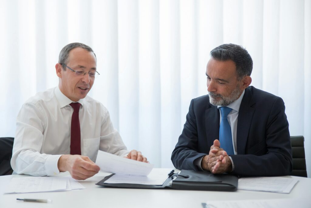 Two middle age white men sitting on a desk reviewing legal documents dressed in suits