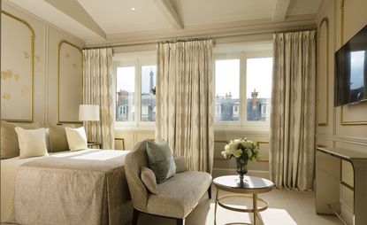 Hotel room with cream and gold walls, bedding and curtains with a safe and table with flowers