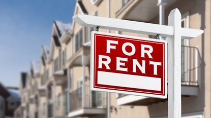 A For Rent sign on a residential street of townhouses.