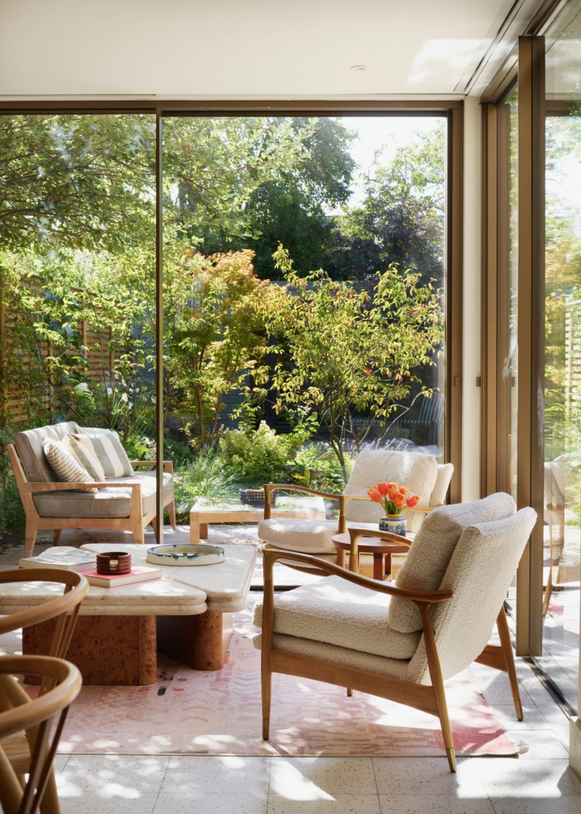 An indoor-outdoor seating area as part of a modern kitchen extension with cream fabrics and natural wood accents with full-height sliding glass doors leading to a seating area outside too