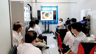 Doctors and patients in a medical room watching a Philips UHD display.