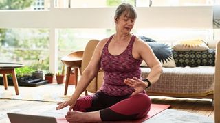 Post menopausal woman doing yoga sitting down on floor in the living room