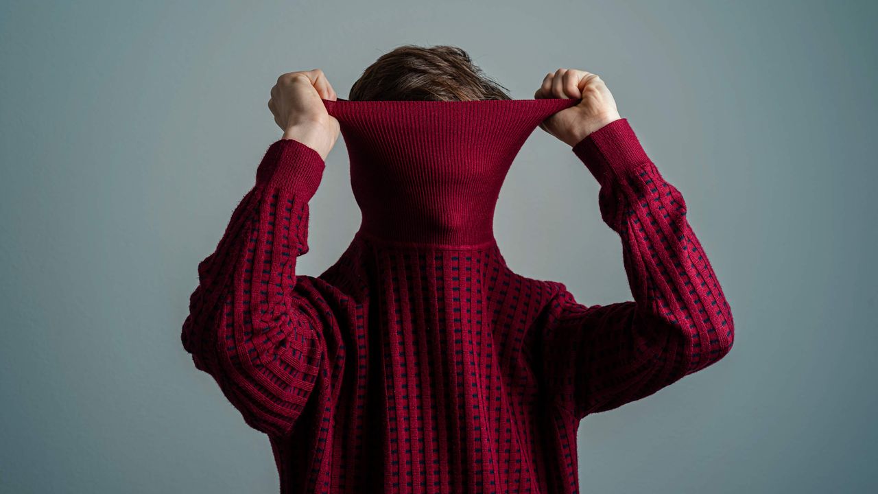 A person pulls the neck of a turtleneck up over their face.