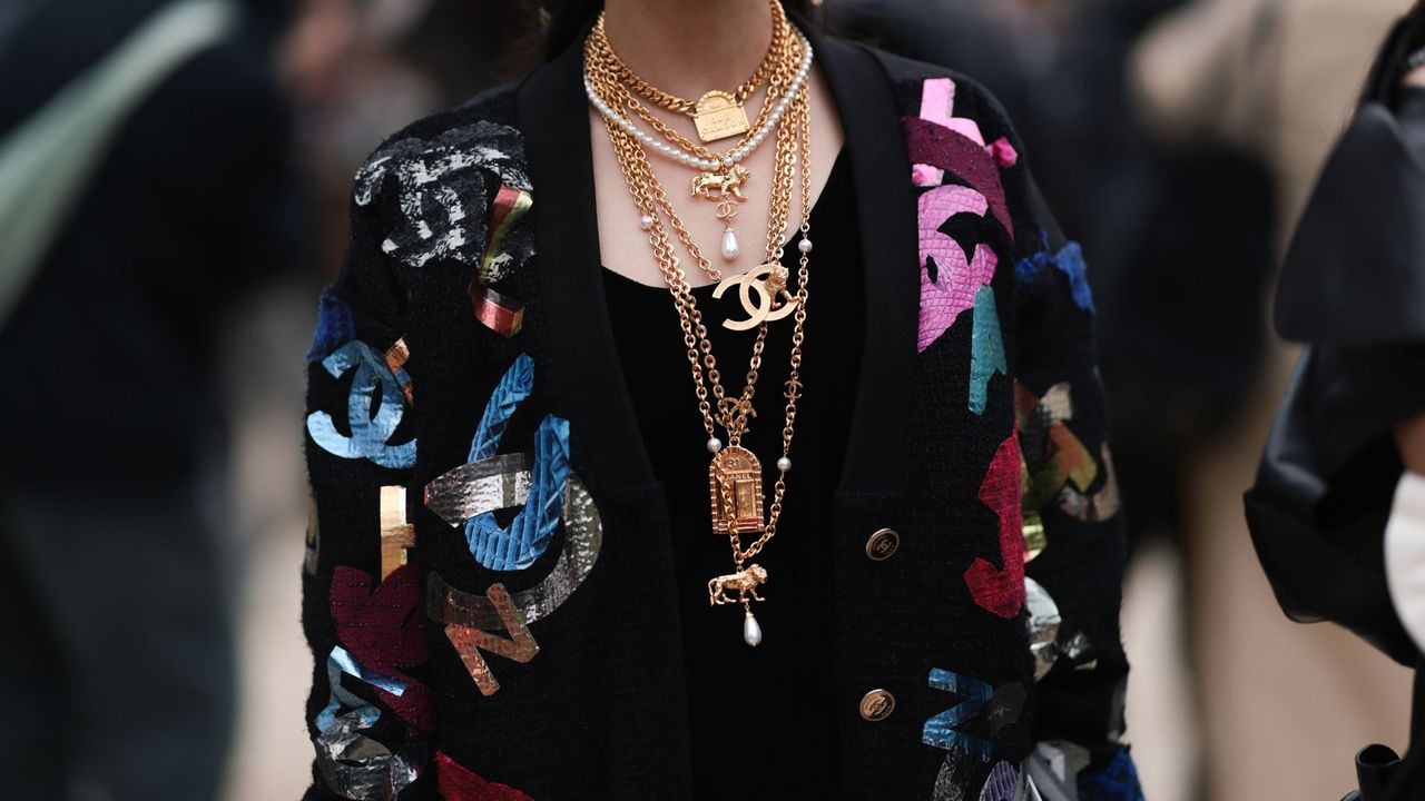 Guest outside of Chanel show wearing a black Chanel cardigan and lots of Chanel necklaces