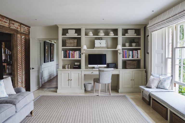 Home office in neutral colours with built in desk and cabinetry, sofa, and window seat