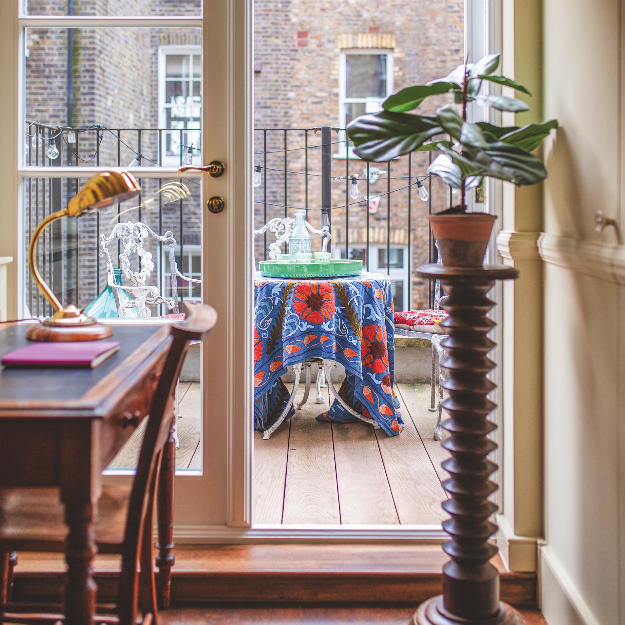 small landing with antique desk and wooden plant stand with access to balcony with garden furniture