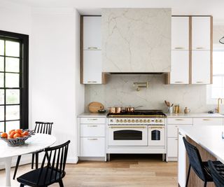 kitchen with white walls, wooden floors and range cooker with marble backsplash and hood