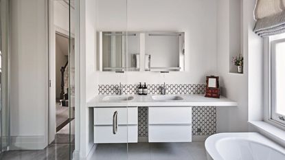 Bathroom decorated in white with double hand basins, white bath and glass doors.