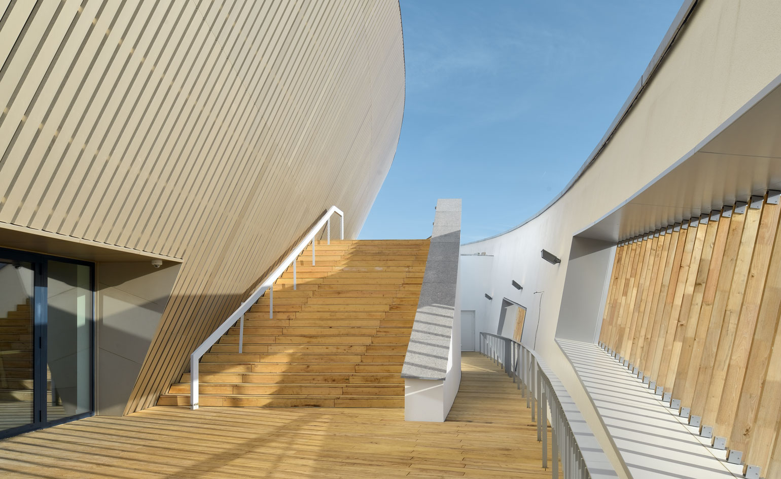 Black framed sliding doors, surrounded by golden brown anodized aluminium and tactile slats of Robinia wood on the external curved walls and stairwell, of the centre building