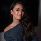 A headshot of Rechelle Balanzat wearing a dark navy off the shoulder top against a black background