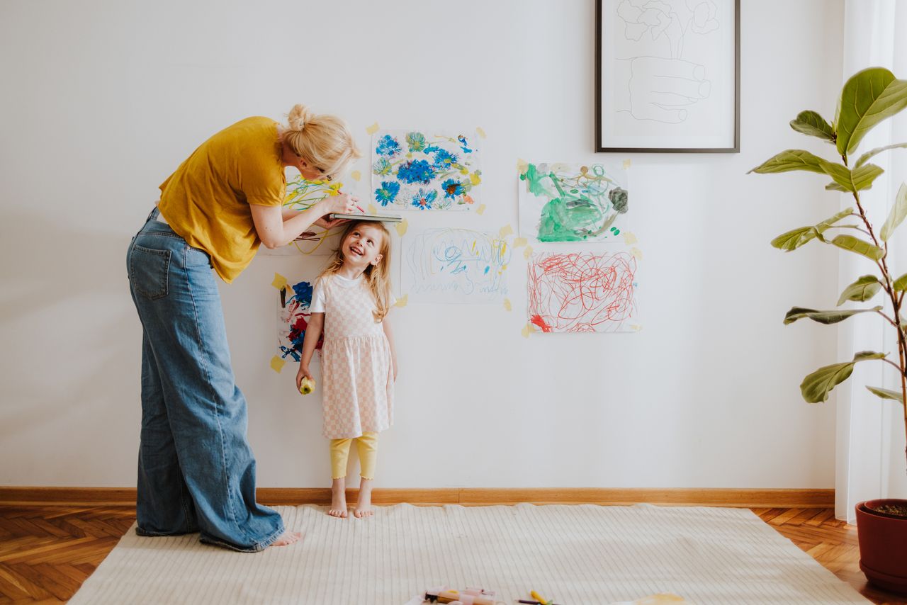 18 summers - mother measuring daughter&#039;s height and marking it on a living room wall 