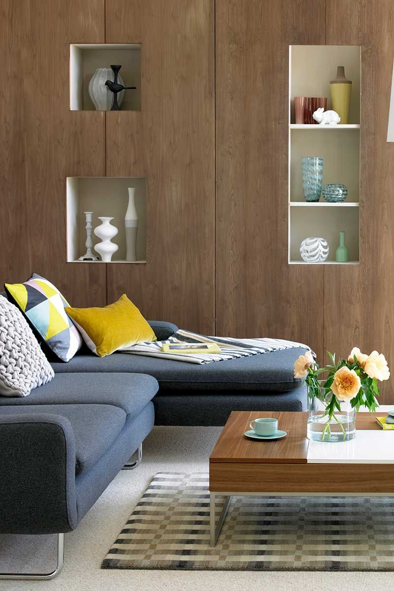 Contemporary living room with wooden wall with display shelves, blue corner sofa, and coffee table