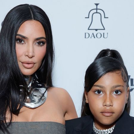 Kim Kardashian wears a bandeau top and shows her bare midriff while posing with daughter North West who is wearing a black suit jacket and choker