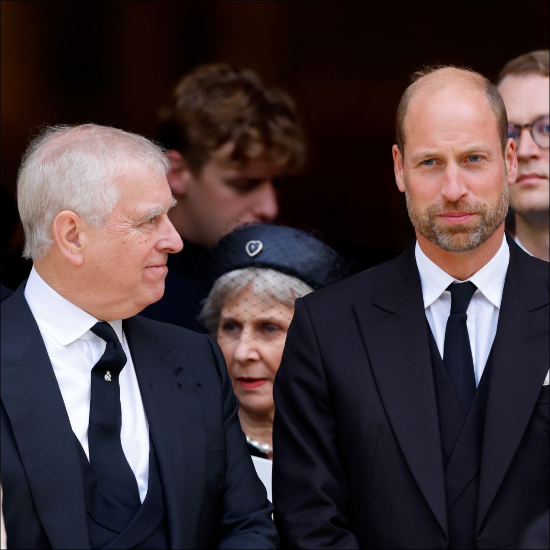 Prince William turns to Prince William and smiles at him, while both wear black suits with black ties and white shirts