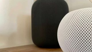 White HomePod mini in front of a black HomePod on a flat surface.