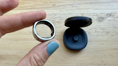 Becca holding the RingConn Gen 3 next to its charging case over a wooden surface