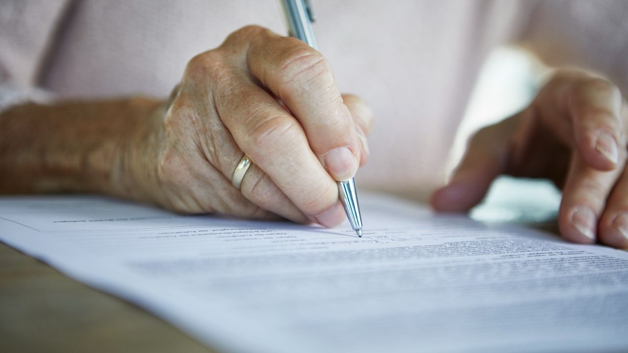 Close-up of a senior woman&#039;s hand signing a document