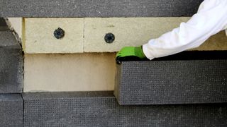 Person putting dark grey external wall insulation block onto wall 