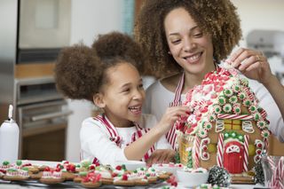 A mother and daughter decorating a gingerbread house happily together.