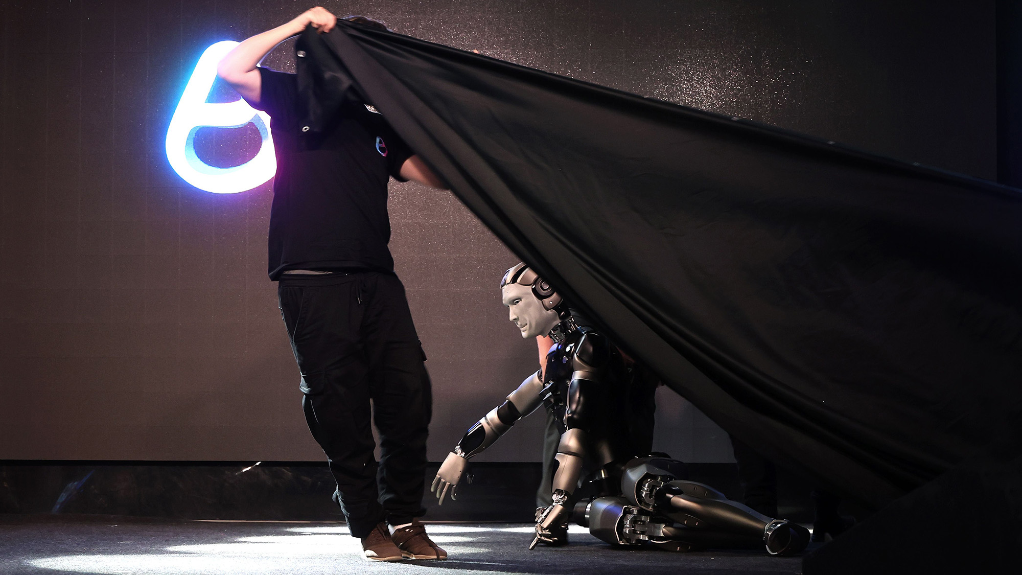 The first Russian anthropomorphic robot &#039;AIDOL&#039; falls on stage during the presentation. A man pulls a black sheet over the fallen robot.