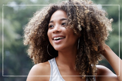 a close up of a girl with curly hair posing next to a tree