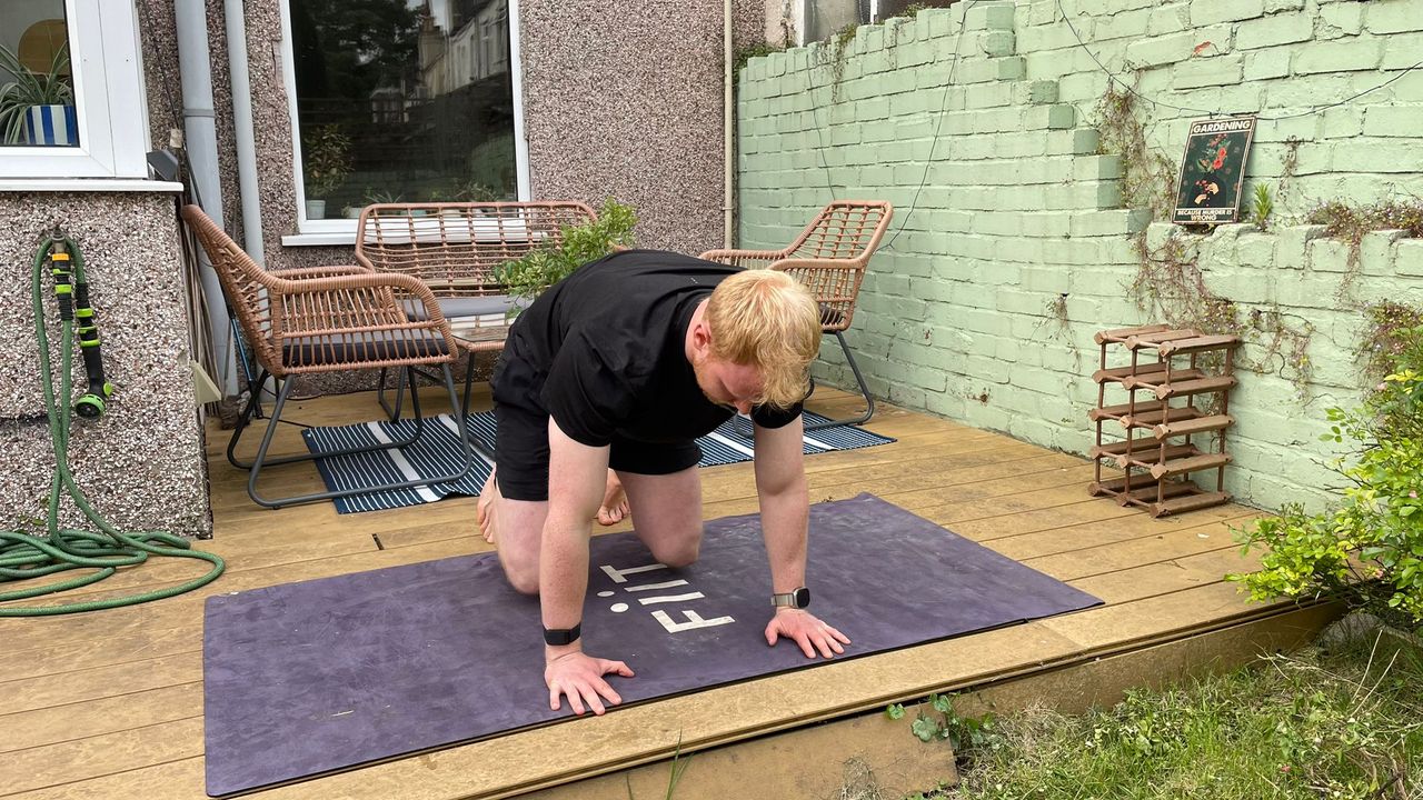 FItness writer Harry Bullmore exercises in his garden on a yoga mat. He is in a tabletop position, with his hands resting on the ground and face pointing down, while his legs are bent at 90 degrees. His knees are slightly elevated off the floor, so all his weight is resting in his toes and hands.