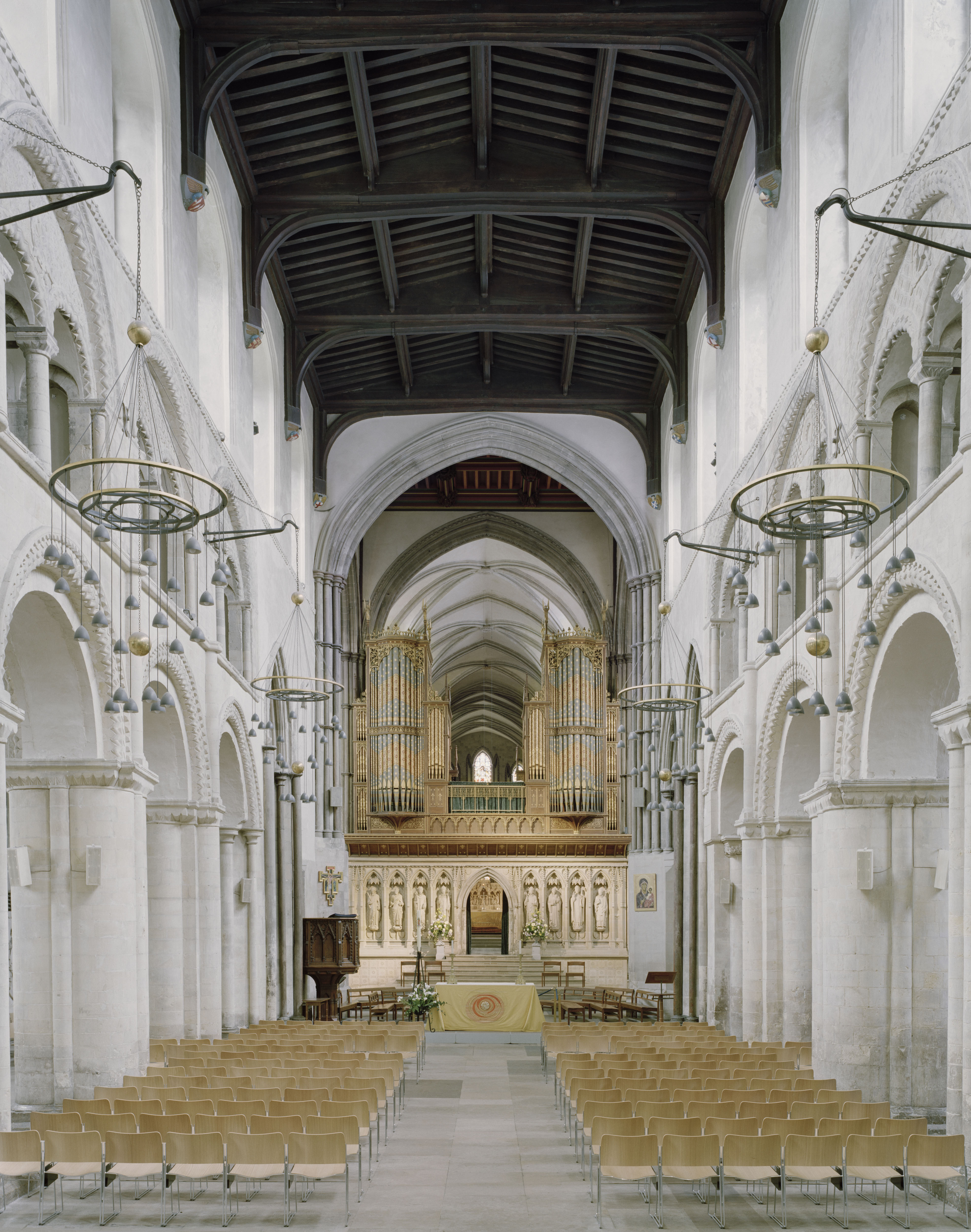 The Romanesque nave of Rochester Cathedral, with round stone arches leading towards the organ pipes and gothic vaulting beyond.