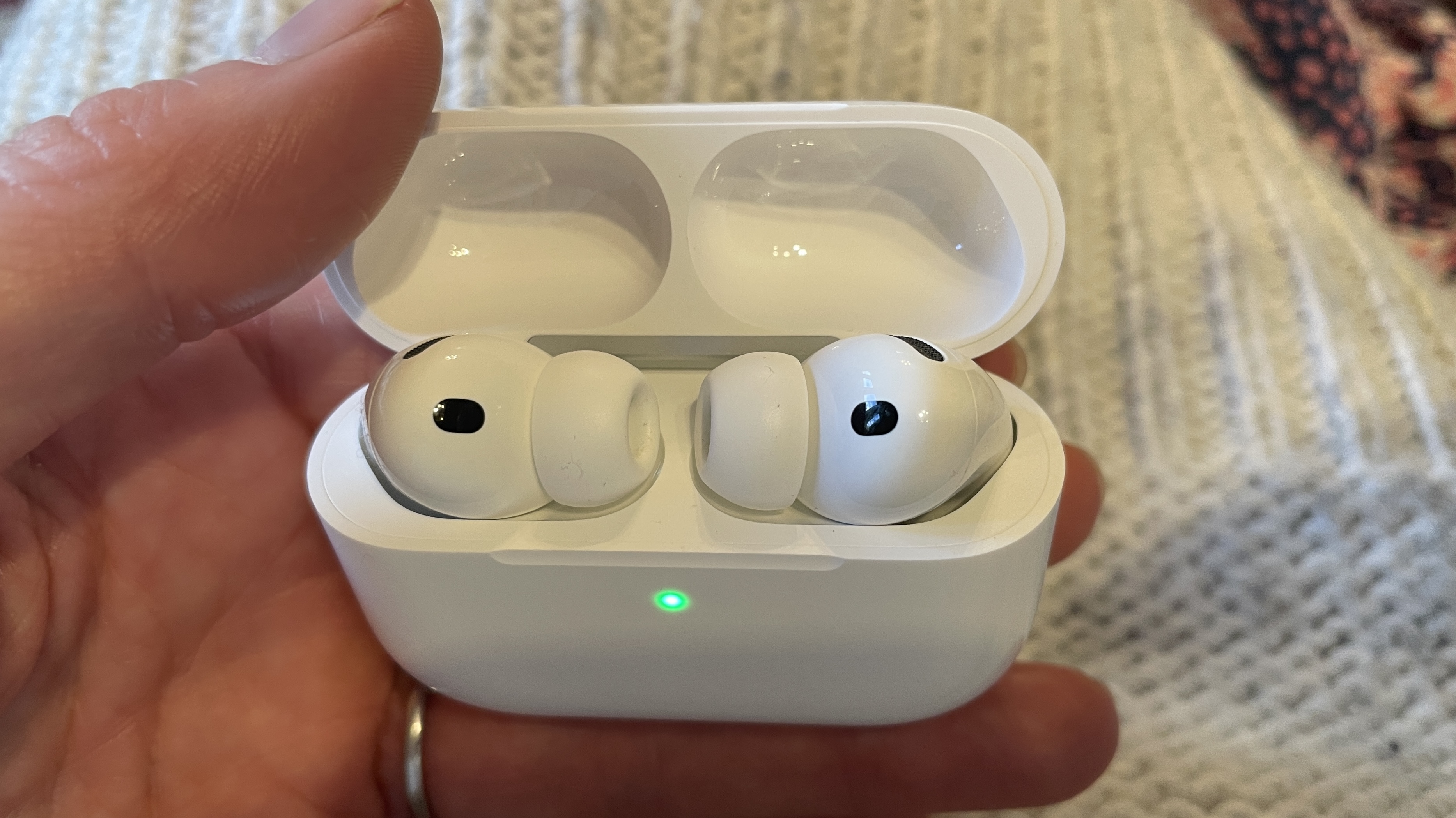 Apple AirPods Pro 3 held in a hand, with beige woollen background
