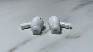 Both 1More PistonBuds Pro Q30 buds lying on a marble effect desktop. The top of the earbud has a microphone, and the speaker and silicone tip are toward the front. The left earbud post shows the letter L, and the right shows the letter R.