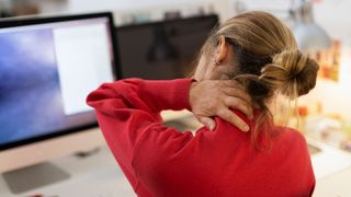 Woman touching the back of aching next sitting at desk with computer
