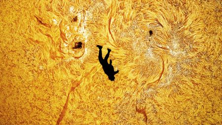 A close up image of the silhouette of a skydiver against the fiery surface of the sun