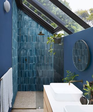 Blue tiled shower in the eaves of a small bathroom with glass roof
