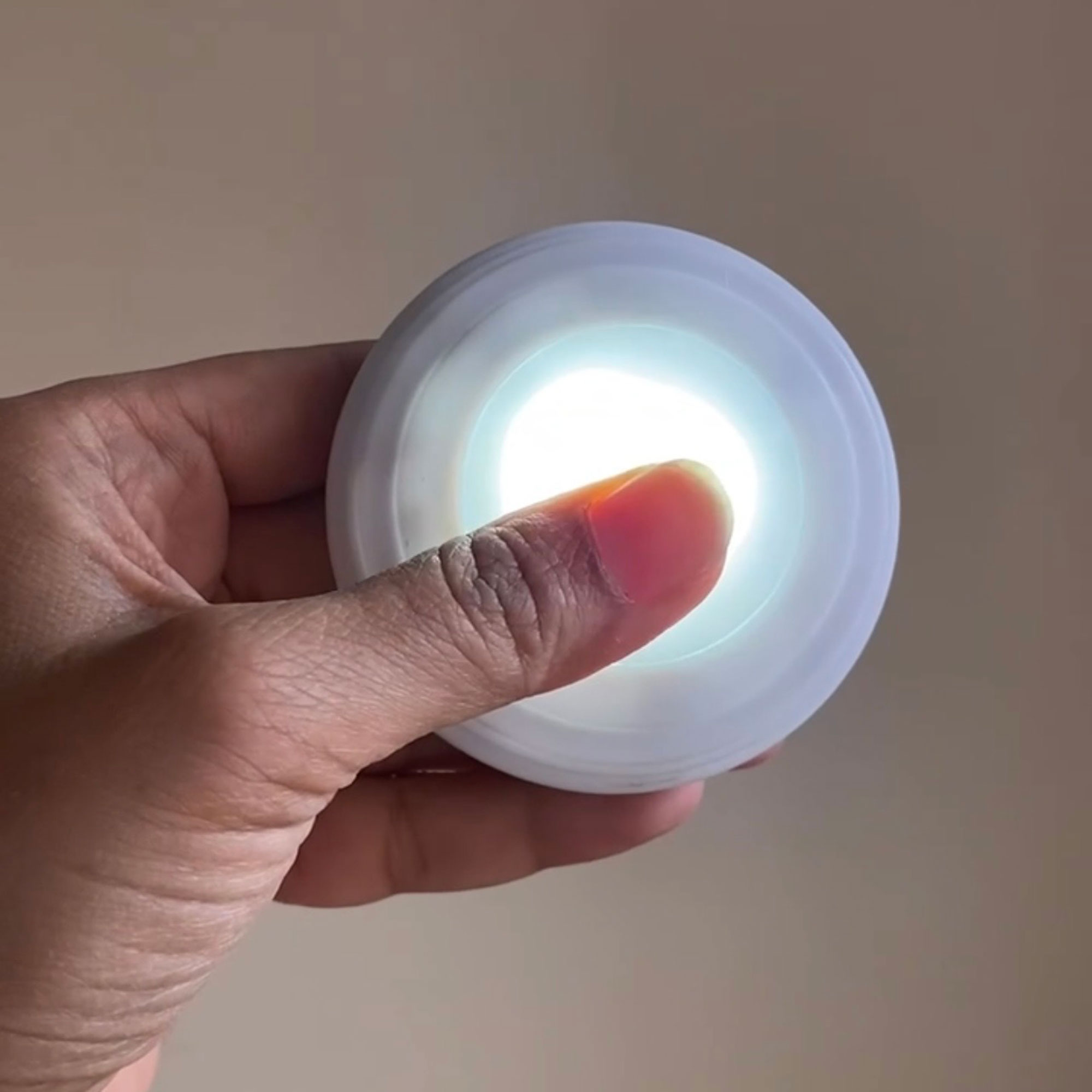Person holding small, switched on puck light