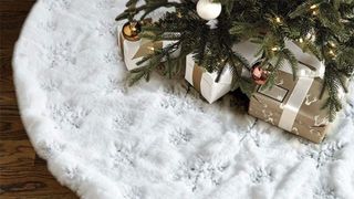 A white christmas tree skirt with embroidered snowflakes in silver, and wrapped presents on top of it.