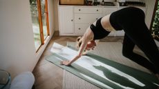 Woman doing Pilates for swimmers in home studio, going into four-point pose on yoga mat with sunlight coming through window
